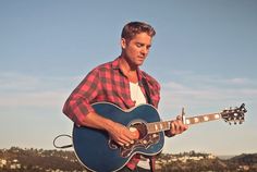 a man holding a blue guitar while standing on top of a hill