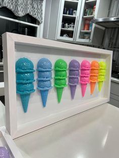 four ice cream cones are in a white frame on a counter top, and one is painted multicolored