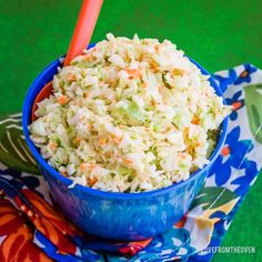 a blue bowl filled with coleslaw on top of a colorful cloth next to an orange spoon