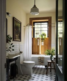 a white toilet sitting next to a bath tub in a bathroom under a window with potted plants