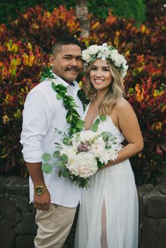 a bride and groom standing next to each other in front of some bushes with flowers