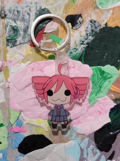 a keychain with a cartoon character on it sitting in front of some paint