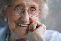 an older woman wearing glasses and smiling for the camera with her hand on her chin