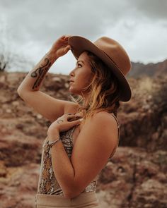 a woman wearing a brown hat and tan skirt standing in front of some rocky terrain