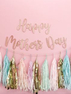 a happy mother's day banner with tassels and streamers on a pink background