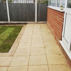 a back yard with a brick walkway and green grass in the foreground, next to a fence