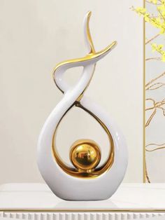 a white and gold sculpture sitting on top of a table next to a vase with yellow flowers