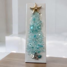 a small christmas tree made out of glass beads on a wooden table with a starfish ornament