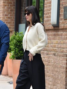 a woman walking down the street wearing black pants and a white sweater with her hands in her pockets