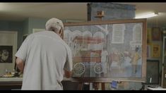 an older man is standing in front of a easel and looking at a painting