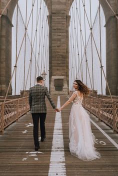 a bride and groom holding hands while walking across the brooklyn bridge on their wedding day