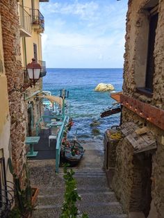 an alley way leading to the ocean with stone buildings and stairs going up one side