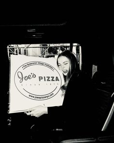 a woman sitting on a bus holding up a sign that says joe's pizza