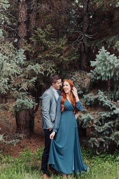 a man and woman standing next to each other in front of some trees with their arms around each other