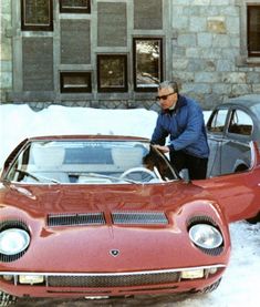 a man standing next to a red car in the snow