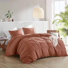 a bed with an orange comforter and pillows in a room next to a potted plant