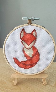 a cross stitch fox sitting on top of a wooden table