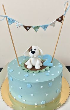 a blue cake with a dog on top and bunting flags in the air above it