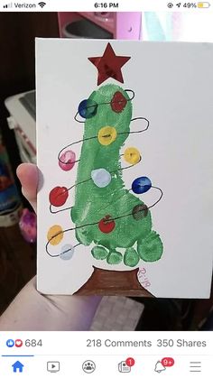 a child's hand holding up a christmas card with a tree drawn on it