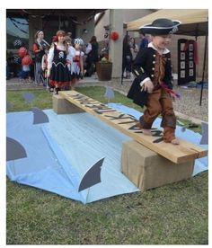 a young boy in pirate costume standing on a cardboard ramp with other children dressed as pirates