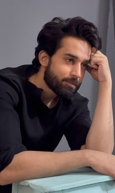 a man sitting at a table with his hand on his head and looking off to the side