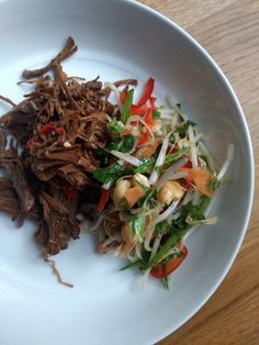 a white plate topped with meat and veggies on top of a wooden table