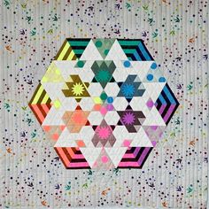 a quilted wall hanging on the side of a white wall with multicolored designs