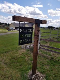 a black river ranch sign in front of a fenced in field with a house