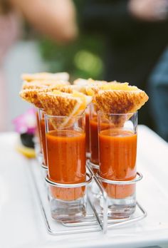 three shot glasses filled with orange juice and garnishes on a white tray