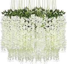 an arrangement of white flowers and greenery hanging from a long rod on a wall