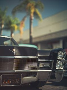 an old black car parked in front of a building with palm trees on the side