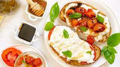 an open face sandwich with tomatoes, mozzarella and basil leaves on a white plate