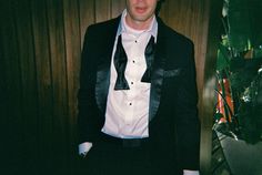 a man in a tuxedo standing next to a plant