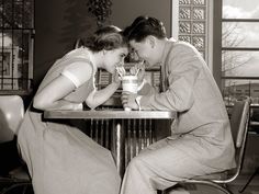 black and white photograph of two people sitting at a table with drinks in front of them