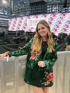 a woman standing in front of a stage wearing a green jacket with flowers on it