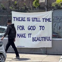 a man walking past a sign that says there is still time for god to make it beautiful