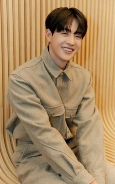 a young man sitting on top of a wooden bench wearing a coat and smiling at the camera