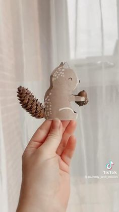 a hand holding a paper cutout of a squirrel with pine cones on its tail