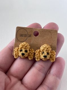 a hand holding a pair of earrings with a poodle design on the front and back