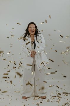 a woman standing in front of gold confetti on a white background with her arms outstretched