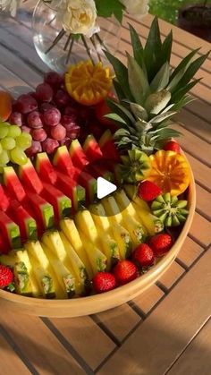 a bowl filled with lots of fruit on top of a wooden table next to flowers