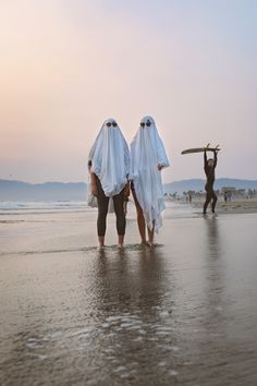 two people walking on the beach with their surfboards in their hands and one person carrying something behind them