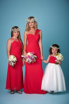 three women in red dresses standing next to each other with flowers on their head and holding hands