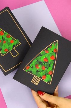 someone is holding up two cards that have christmas trees on them, one has green leaves and the other has red berries