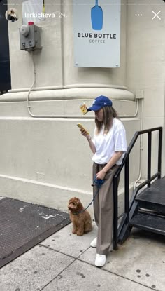 a woman is standing on the sidewalk with her dog and looking at something in her hand