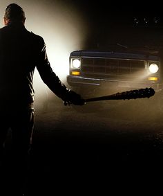 a man holding a baseball bat in front of a truck on a foggy road