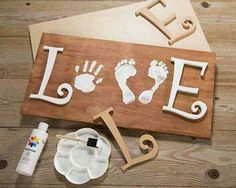 a wooden sign that says love with two baby feet and one handprint on it