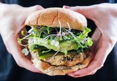 a person holding a sandwich with lettuce and other vegetables on it in their hands