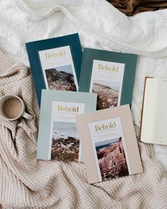 three books on a bed next to a cup of coffee and an open book with the title behold