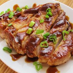 some meat with sauce and green onions on a white plate